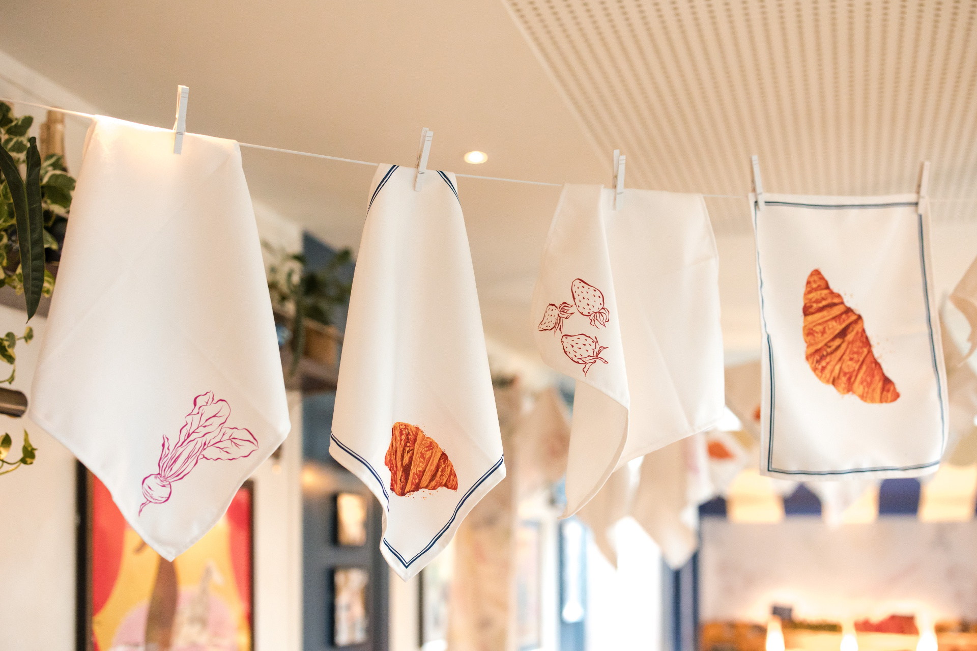 Printed napkins pegged to a line inside the restaurant, illustrated with beetroot, croissants and strawberries.