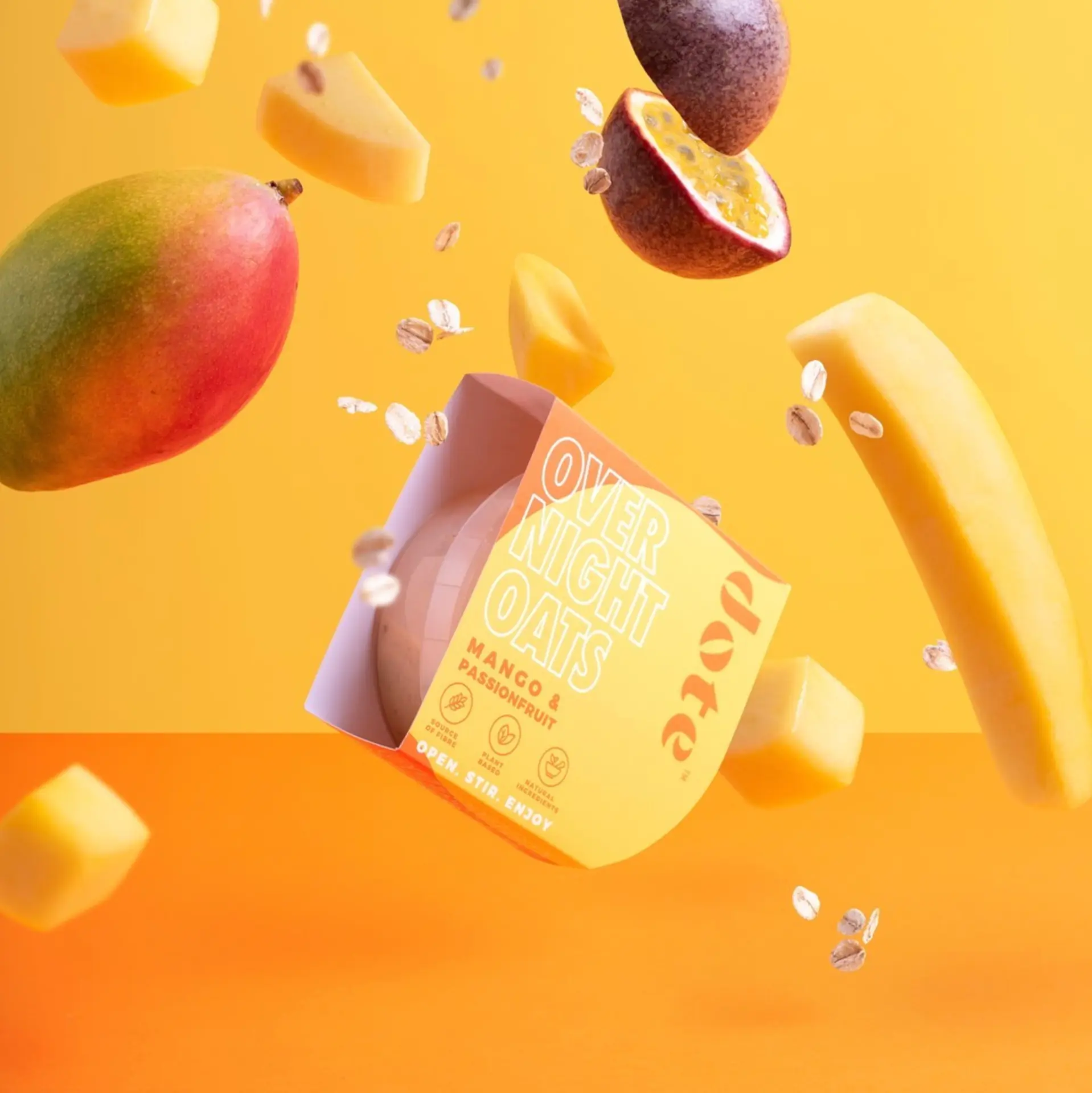 Dote mango and passionfruit overnight oats pot suspended among falling mango pieces, passionfruit and oats on yellow.